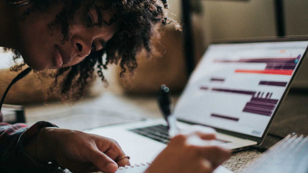 Focused woman writing in a notebook beside a laptop during a long, productive work session